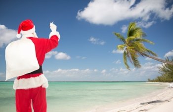 christmas, holidays, travel and people concept - man in costume of santa claus with bag writing something from back over tropical beach background
