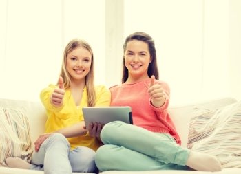 friendship, technology and internet concept - two smiling teenage girls with tablet pc computer at home showing thumbs up