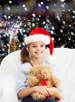holidays, presents, christmas, childhood and people concept - smiling little girl with teddy bear toy over snowy night city background