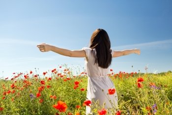 happiness, nature, summer, vacation and people concept - young woman dancing on poppy field from back