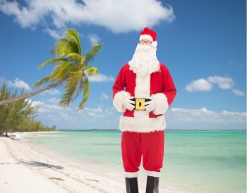 christmas, holidays, travel and people concept - man in costume of santa claus over tropical beach background over tropical beach background