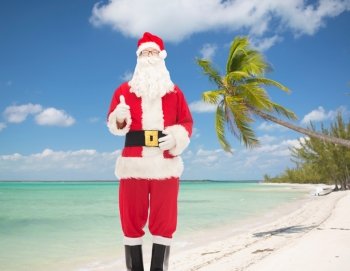 christmas, holidays, gesture, travel and people concept- man in costume of santa claus showing thumbs up over tropical beach background
