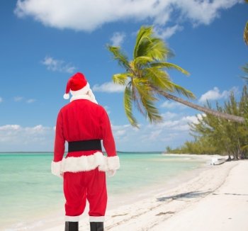 christmas, holidays and people concept - man in costume of santa claus from back over tropical beach background