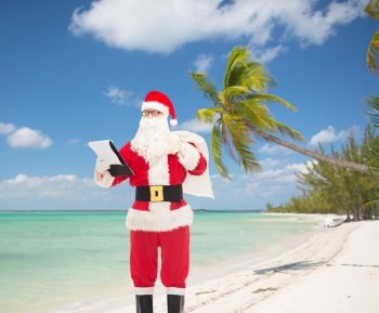 christmas, holidays, travel and people concept - man in costume of santa claus with notepad and bag over tropical beach background