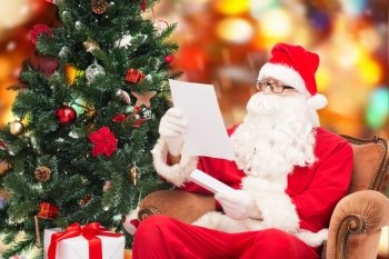 christmas, holidays and people concept - man in costume of santa claus with letter and christmas tree sitting in armchair over red lights background