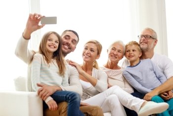 family, happiness, generation and people concept - happy family sitting on couch and making selfie with smartphone at home