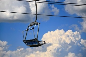 Empty ski lift chair above clouds and sky