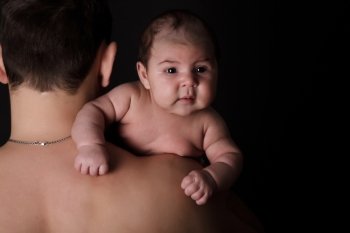 Newborn baby on father’s shoulder on black