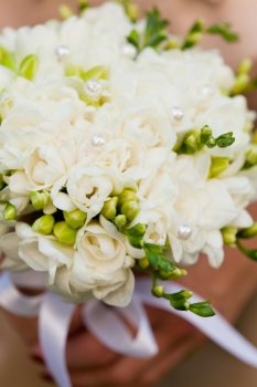 Wedding bouquet from white freesias closeup in bride’s hands
