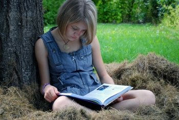 Girl read book under the tree, on the hay. It’s summer