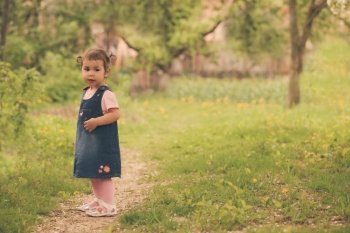 Little adorable girl in the garden, walks on the path