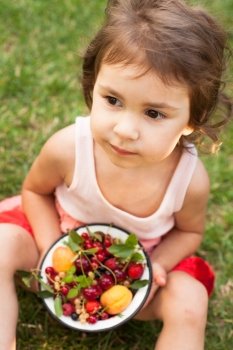 Little girl holds a bowl with summer fruits