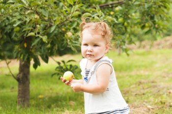 Pretty little girl holding an apple in hand, standing under the apple tree