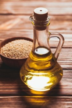 Sesame oil in a glass bottle with a cork and heap sesame seeds in a wooden bowl. The sesame oil