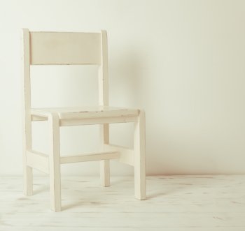 Single white rustic chair standing in an empty room on light wooden parquet floor.. White old-fashioned chair 