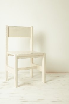 Single white rustic chair standing in an empty room on light wooden parquet floor.. White old-fashioned chair 