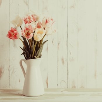 White vase with delicate shades armful of tulips on a wooden background. Flowers bouquet of white and pink tulips