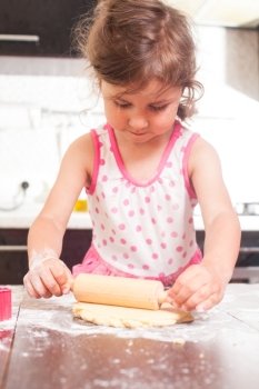 Little cute girl stretching the dough in the kitchen. Happy little chef 
