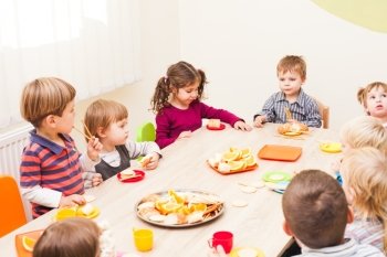 Children are sitting at the table with lunch and eating fruits and cakes. Lunch in kindergarden