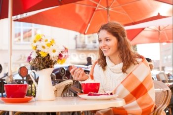 Woman is sitting in cafe outdoor and eat cake and cocoa, cozy autumn