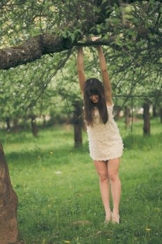 Pretty girl playfully hangs on a tree branch with bent legs. Girl clings to a tree branch