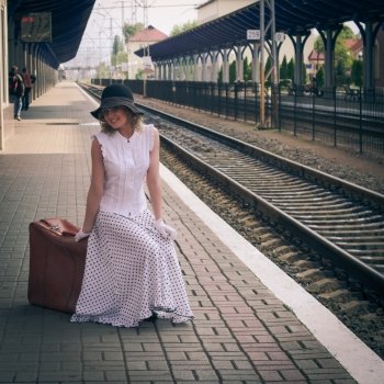 Woman in vintage dress with old suitcase on the railroad station. Woman in vintage dress