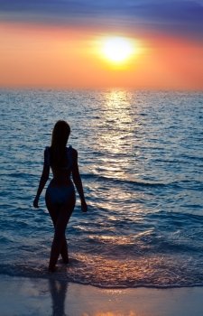 Silhouette of the sexual woman going at ocean towards to a sunset