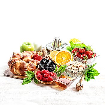 Breakfast table setting with croissants, muesli, fresh berries, fruits orange, apple, milk. Healthy organic food