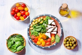 plate of salad with cheese, tomatoes, greens on wooden table, top view