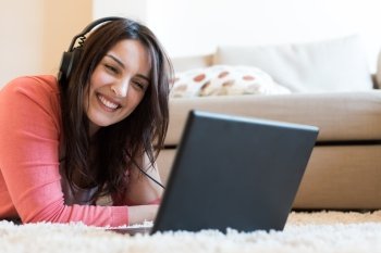Woman lying on the floor using headphones on laptop