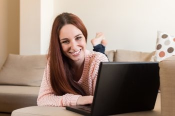 Woman laying down on couch with a laptop