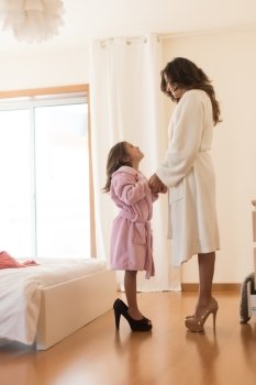 Little girl wearing heels with her mother in bedroom