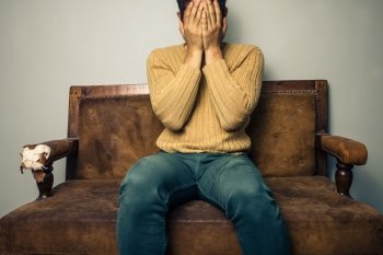 Young man sitting on a sofa covering his face