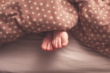 Young woman’s feet in bed under the covers