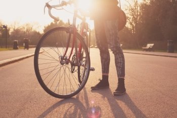 A Young woman is standing with her bicycle in the park at sunset