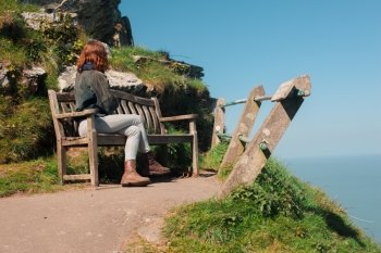 Young woman is sitting on a bench on top of a cliff