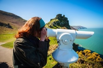Young woman is looking through a telescope by the sea