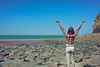 Young woman is raising her arms in joy on the beach