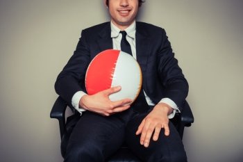 A businessman is sitting in an office chair with a beach ball
