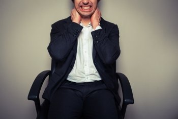 A young businessman sitting in an office chair is having neck pains