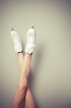 Young woman wearing ice skates with her legs up against a wall