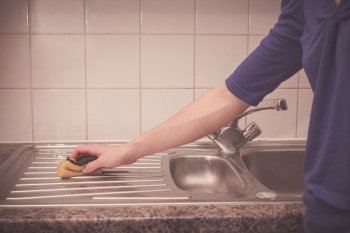 A young woman is cleaning around the kitchen sink
