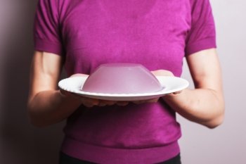 A young woman wearing a purple top is holding a plate with a pudding on it