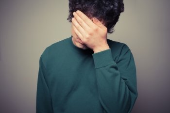 Young man is hiding his face in the palms of his hands