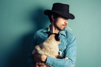 A young cowboy is smoking a cigarette and holding a cat
