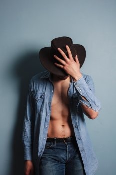 Sexy young cowboy by a blue wall is standing with his shirt open