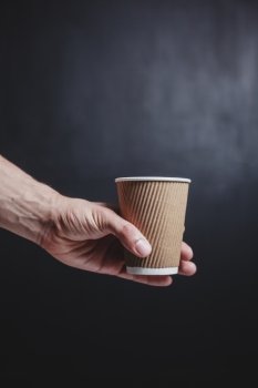 Close up on a young man’s hand holding a brown paper cup