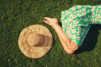 A young woman wearing a dress is sleeping on the grass with a hat next to her