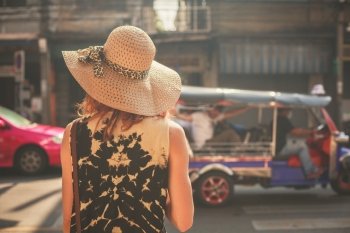 A young woman wearing a hat is walking in the streets of an asian country