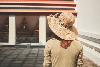 A young woman wearing a hat is exploring a buddhist temple